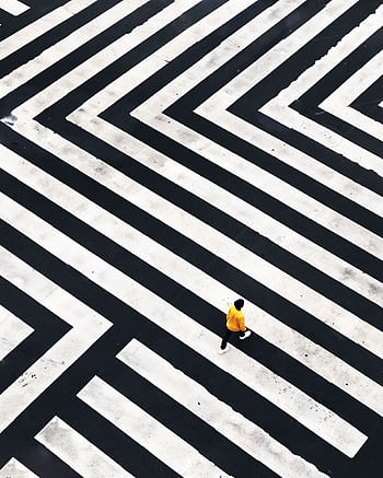 A person in a yellow jacket walks across a striking striped crosswalk from above. HD phone wallpaper