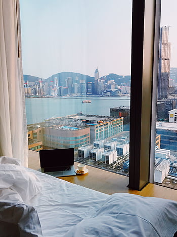 Cozy hotel room with cityscape view from bed, featuring a laptop and coffee by the window. HD phone wallpaper