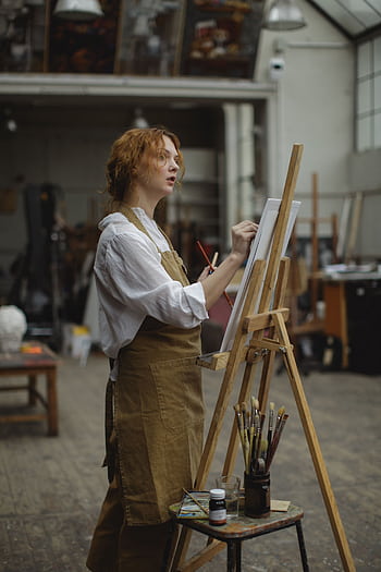 A focused female artist paints on canvas in an art studio, showcasing creativity and skill. HD phone wallpaper