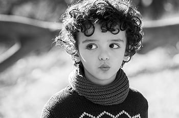 Monochrome of a child with curly hair wearing a scarf and sweater outdoors. HD wallpaper