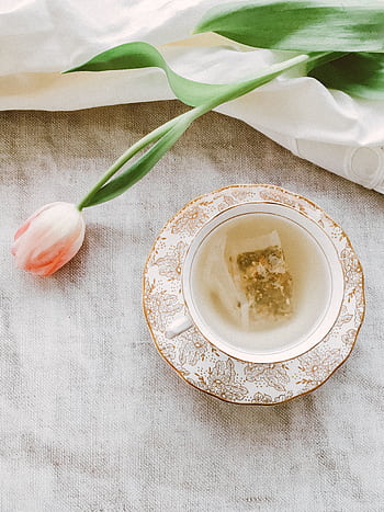 A delicate tea scene with herbal tea in a floral porcelain cup beside a pink tulip. HD phone wallpaper