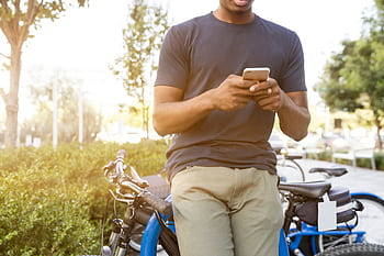 Casual young man leaning on a bike outdoors while using a smart in daylight. HD wallpaper