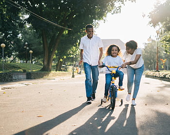 Happy family teaching their child to cycle on a sunny day outdoors. HD wallpaper