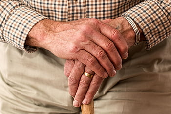 A detailed of elderly hands clasping a wooden cane, symbolizing aging and support. HD wallpaper