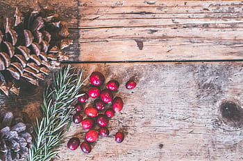 Top view of rustic holiday decor featuring pinecones, cranberries, and rosemary on a wooden surface. HD wallpaper