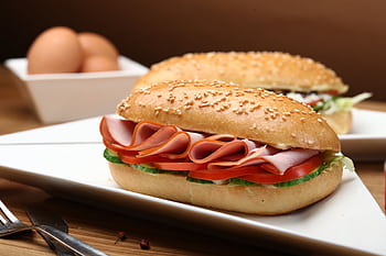 Tasty ham and vegetable sandwich on sesame bun with fresh ingredients served on a white plate. HD wallpaper