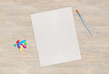 A blank sheet of paper sits on a wooden desk with colorful chalk and a pencil, offering creative possibilities. HD wallpaper