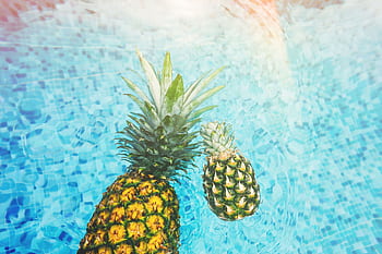 Two vibrant pineapples float in a sunlit swimming pool, embodying summer vibes. HD wallpaper