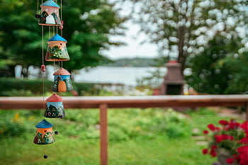 Cute ceramic house ornaments hanging in a vibrant garden setting near water. HD wallpaper