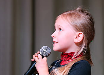 Cute young girl passionately singing into a micro on stage, captured in a close-up profile view. HD wallpaper