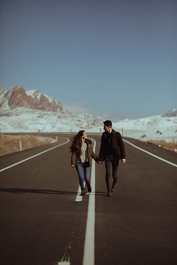 A romantic couple walking hand in hand on a scenic road with snowy mountains in the background. HD phone wallpaper