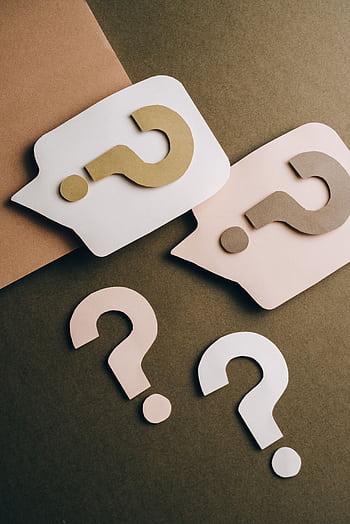 Artistic paper cutouts of question marks creating a conceptual design on a brown surface. HD phone wallpaper