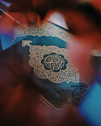 A close-up of a Quran with ornate Arabic calligraphy, surrounded by a blurred artistic effect. HD phone wallpaper