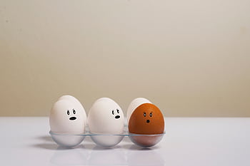 A creative depiction of eggs with facial expressions in a tray, symbolizing diversity. HD wallpaper
