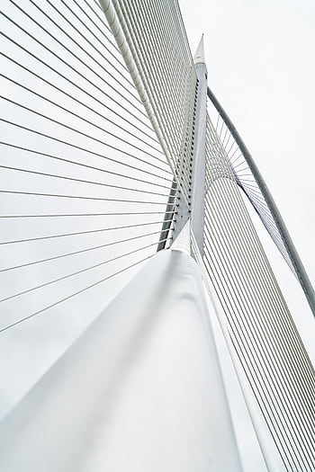 Low angle view of a modern suspension bridge with steel cables and architectural lines under a cloudy sky. HD phone wallpaper