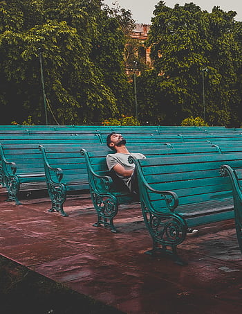 A man enjoys solitude on a series of teal benches in a lush park. HD phone wallpaper