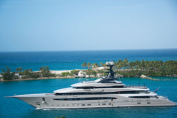 High-end yacht cruising along a tropical coastline with clear blue waters and lush greenery. HD wallpaper