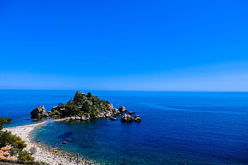 A que view of a rocky island surrounded by clear blue ocean waters and a serene beach shoreline. HD wallpaper