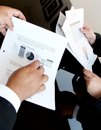 A business team reviewing charts and graphs on documents, emphasizing data analysis and teamwork. HD phone wallpaper