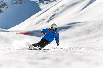 A skier carves down a sunlit snowy slope wearing protective gear. Perfect for winter sports themes. HD wallpaper