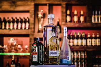 A stylish display of various liquor bottles on a bar shelf with a blurred background. HD wallpaper