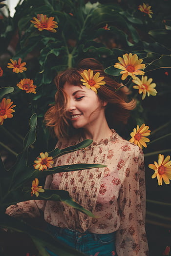 A young woman in a floral dress smiles among vibrant yellow flowers, creating a serene outdoor portrait. HD phone wallpaper