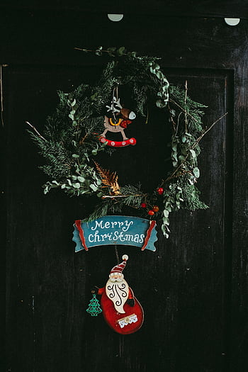 Close-up of a rustic Christmas wreath on a dark door with seasonal decorations. HD phone wallpaper