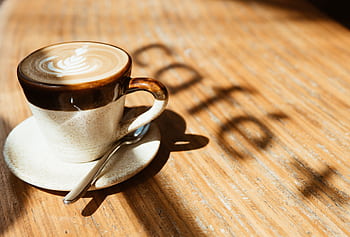 A warm cappuccino with latte art basking in morning sunlight on a wooden table. HD wallpaper