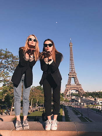 Two stylish women pose in front of the Eiffel Tower in Paris, symbolizing friendship and travel. HD phone wallpaper