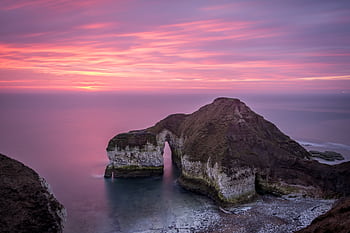 Serene seascape featuring a natural arch at sunset with pink and purple skies. HD wallpaper