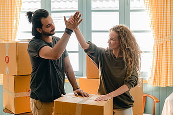 A cheerful couple celebrating their move into a new home, surrounded by boxes. HD wallpaper