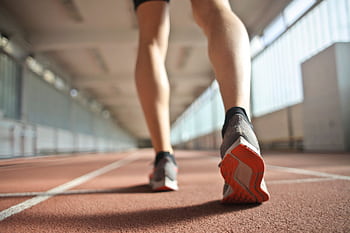 Back view of a runner's legs in a stadium, focusing on footwear and athletic motion. HD wallpaper