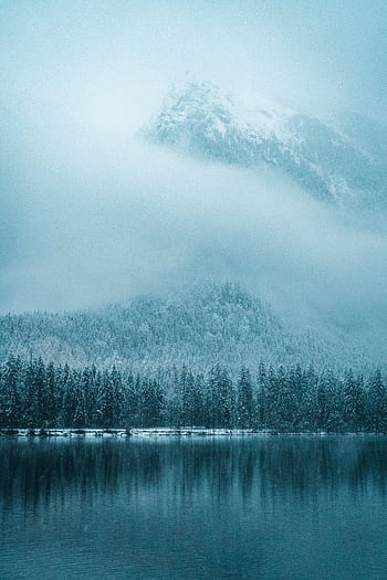 A tranquil winter scene of snow-covered mountains and a reflective lake in Ramsau, Germany. HD phone wallpaper