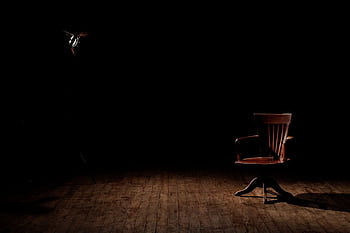 A vintage wooden chair is spotlighted in a dark studio setting, casting shadows. HD wallpaper