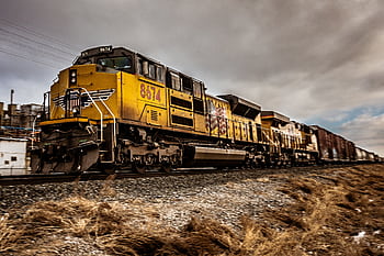 Dynamic shot of a yellow train moving on railway tracks under cloudy skies. HD wallpaper