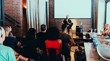 A dynamic seminar with a speaker engaging a diverse audience in a modern indoor setting. HD wallpaper
