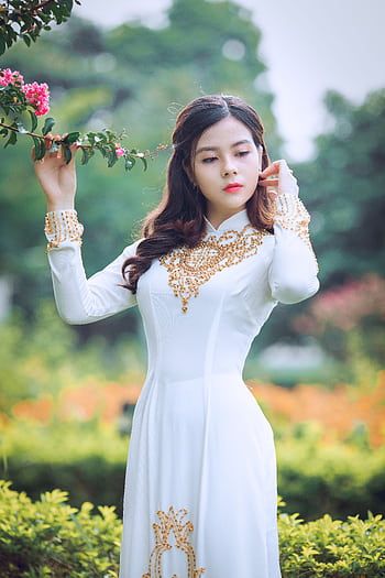 Elegant woman in white Ao Dai standing gracefully in a lush garden setting. HD phone wallpaper