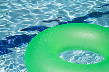 A vibrant green inflatable swim ring floating in a refreshing blue swimming pool. HD wallpaper