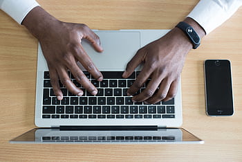 Person typing on a laptop with a smart nearby, showcasing modern technology use. HD wallpaper
