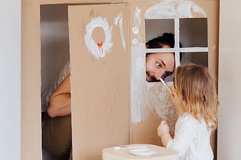 Father and daughter enjoying creative bonding by painting a cardboard playhouse indoors. HD wallpaper