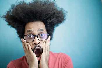 Close-up portrait of a surprised man with afro hairstyle and glasses against a blue background. HD wallpaper