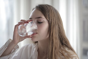 A woman enjoying a refreshing glass of water indoors during the day. HD wallpaper