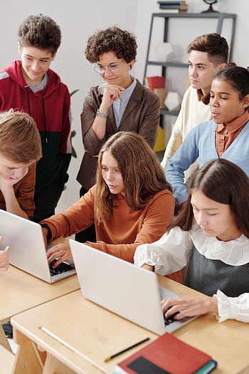 Group of teenagers in a classroom collaboratively working on laptops, fostering team learning. HD phone wallpaper