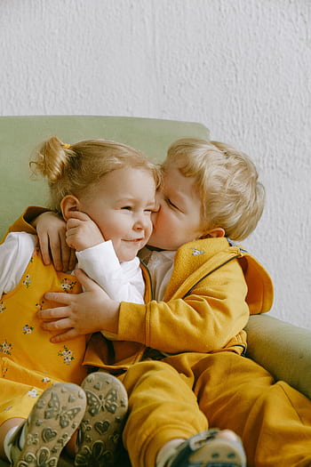 Cute siblings hugging and smiling on an armchair, capturing a tender moment of love. HD phone wallpaper