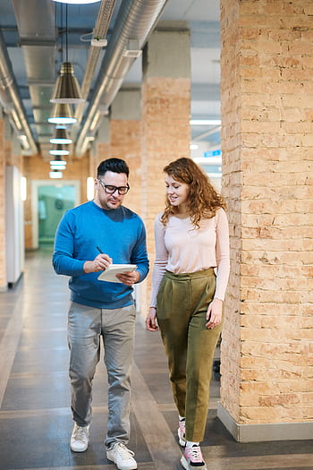 Two business colleagues walking in an office hallway discussing ideas with a notepad. HD phone wallpaper