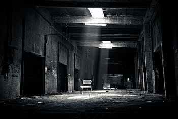 A haunting black and white of an abandoned warehouse with a solitary chair illuminated by sunlight through a window. HD wallpaper
