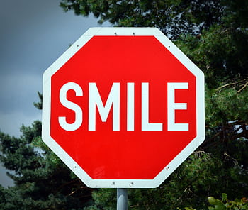 A playful red stop sign with the word 'SMILE', surrounded by trees. HD wallpaper