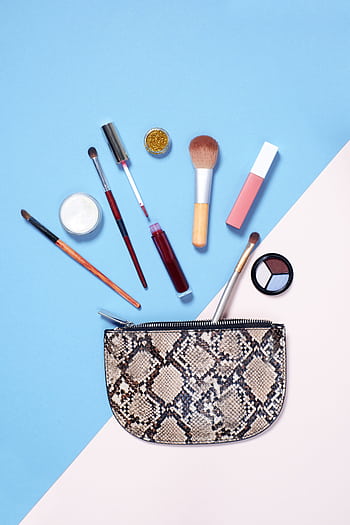A flat lay of vibrant makeup items arranged around a stylish snakeskin cosmetic bag on a blue and beige background. HD phone wallpaper