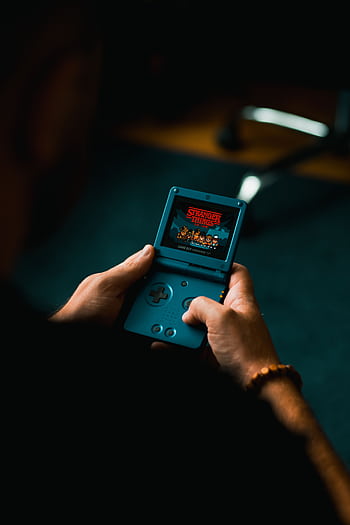 Close-up of individual holding a retro handheld gaming device, playing a classic video game indoors. HD phone wallpaper