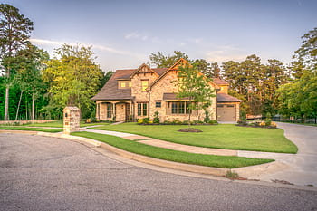 Elegant stone family home with manicured lawn, trees, and driveway on a sunny day. HD wallpaper